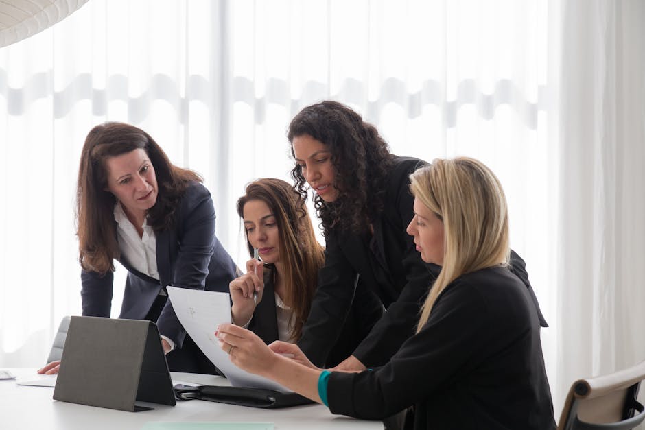 Home Four businesswomen engaged in discussion over documents in a contemporary office setting.
